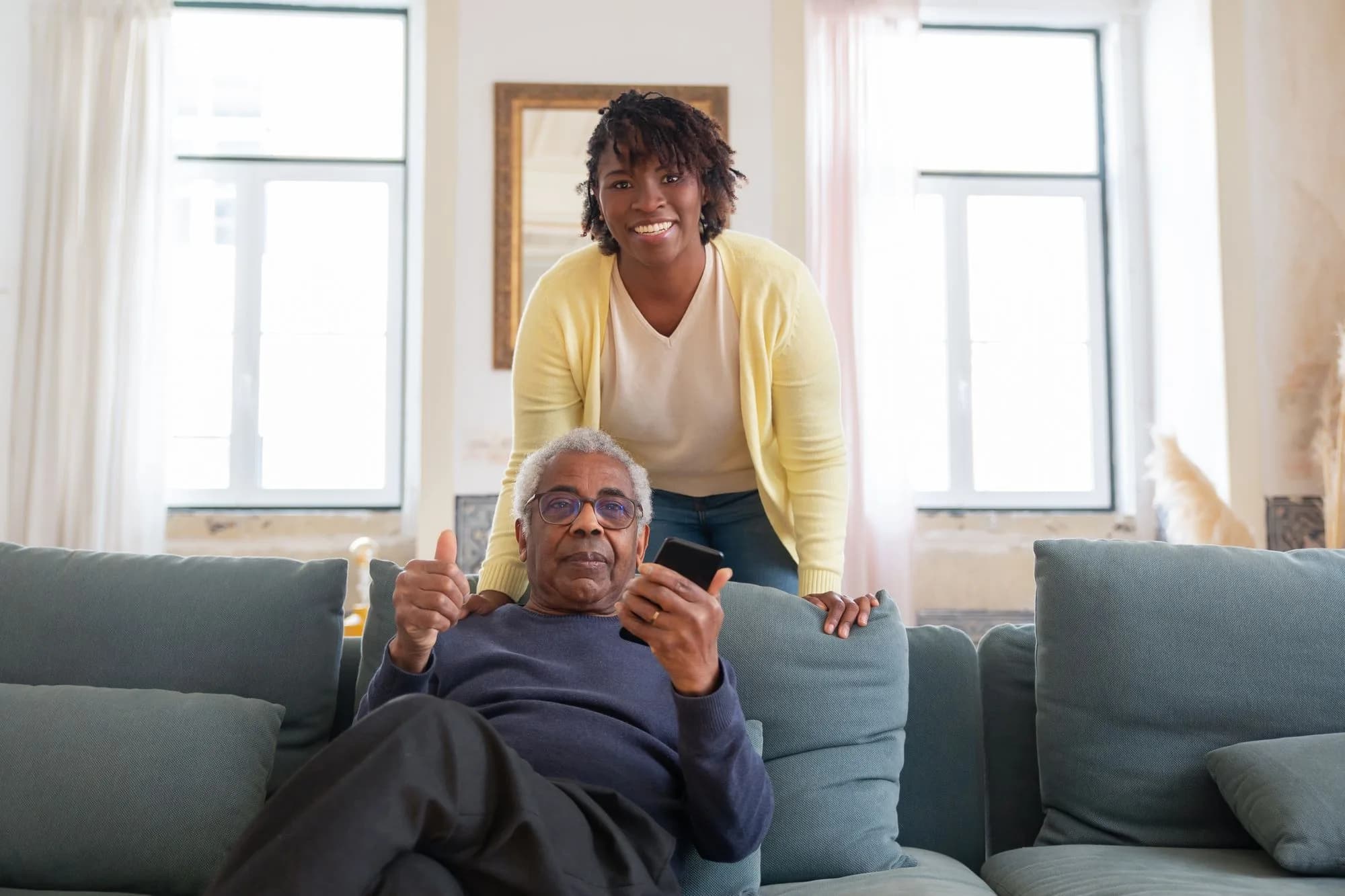 An older man and a younger woman sitting together on a sofa at home, both smiling