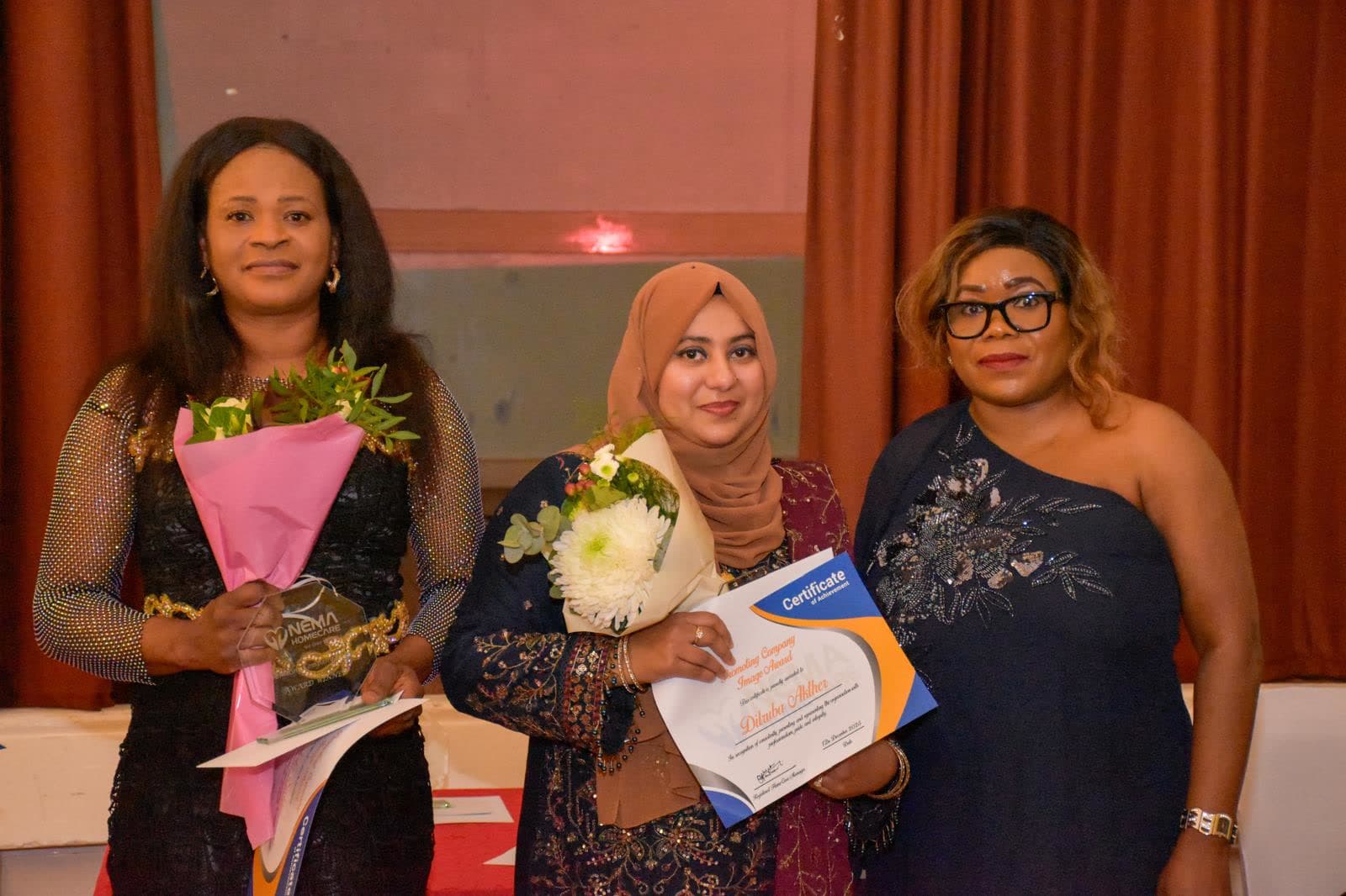 Three Nema staff holding flowers and certificates at an end of year awards evening