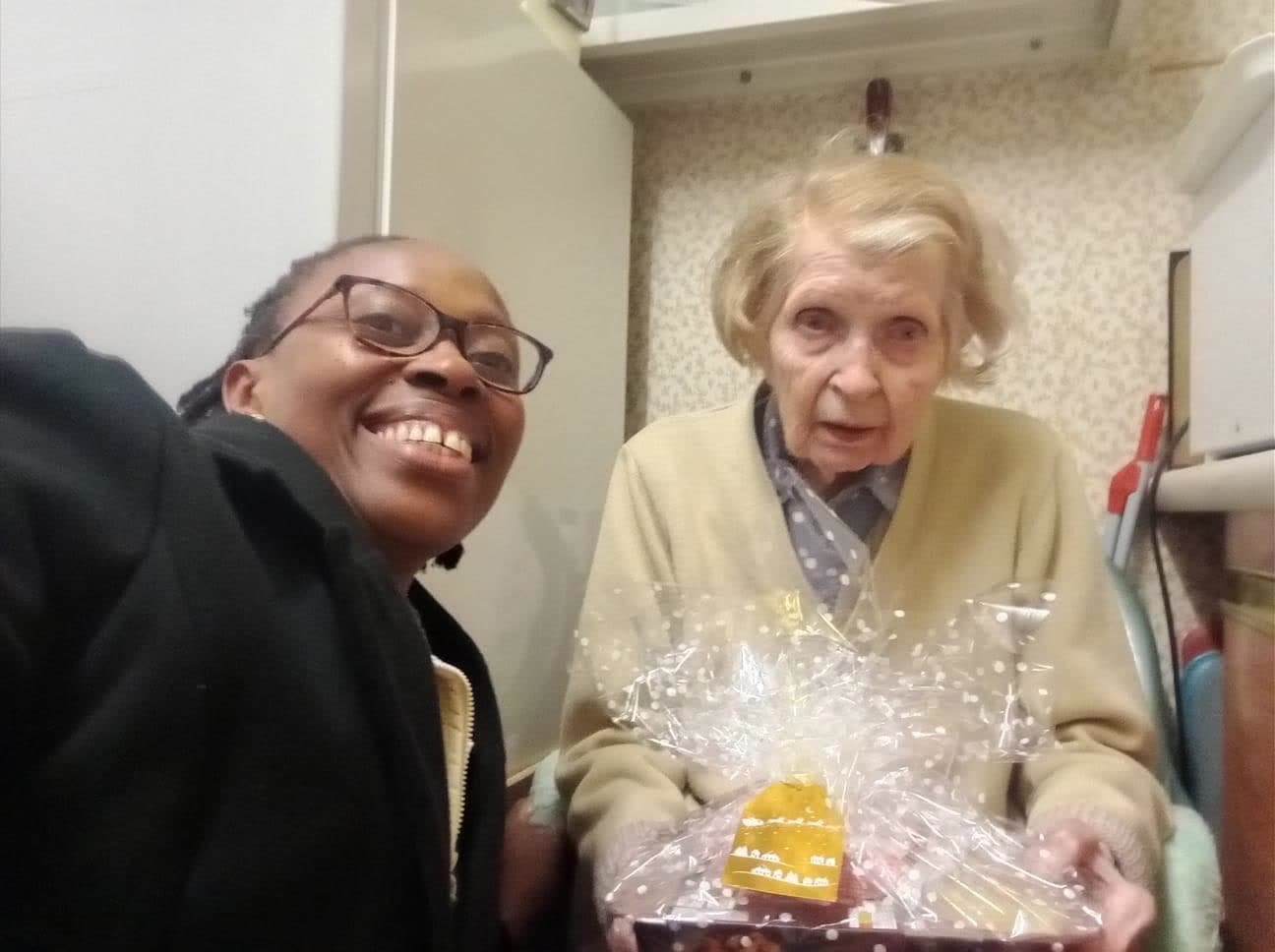 A Nema staff member and an older woman smiling, the woman holding a Christmas hamper