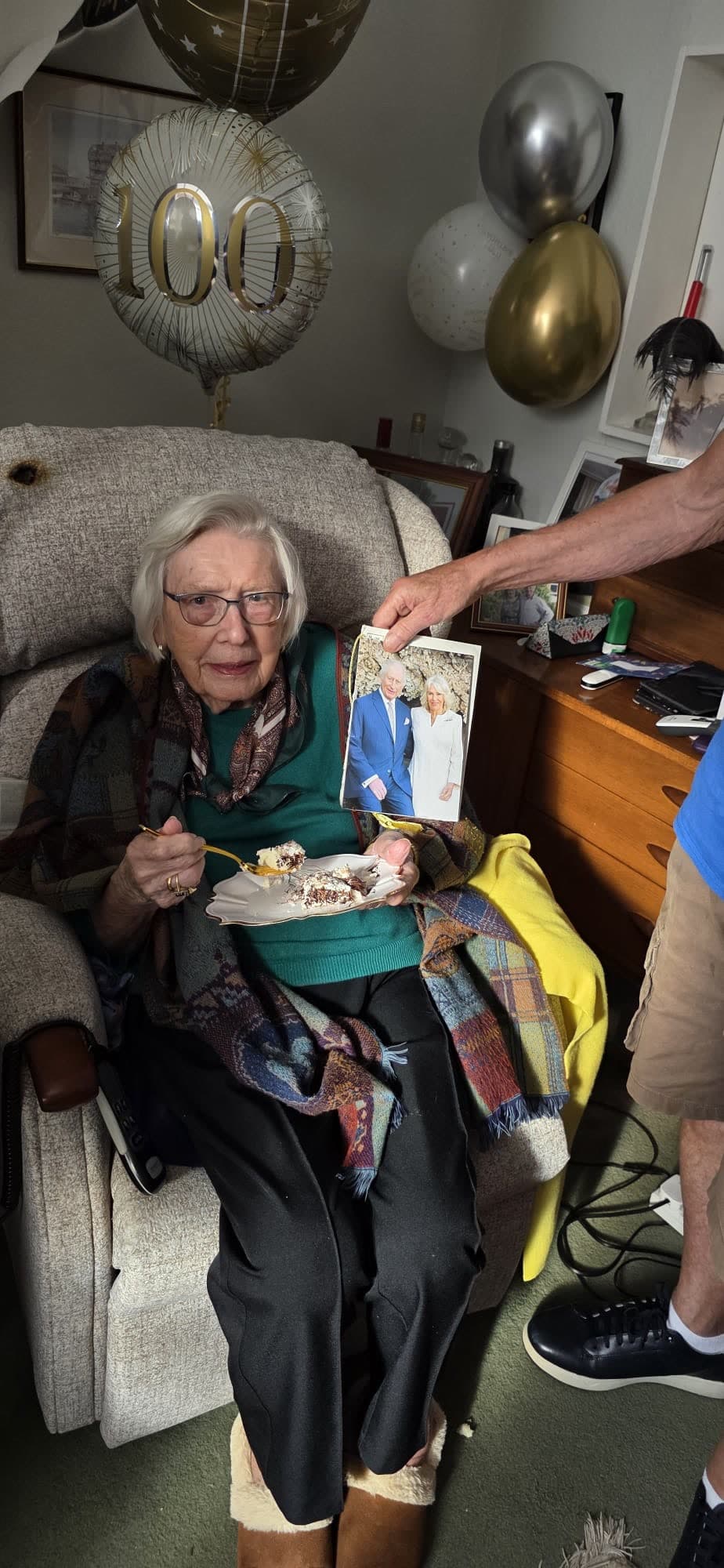 An older woman celebrating her 100th birthday at home, with balloons and cards